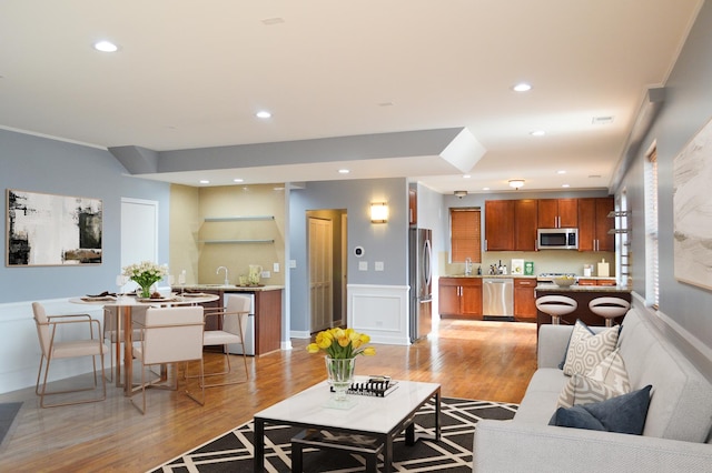 living room featuring sink, crown molding, and light hardwood / wood-style flooring