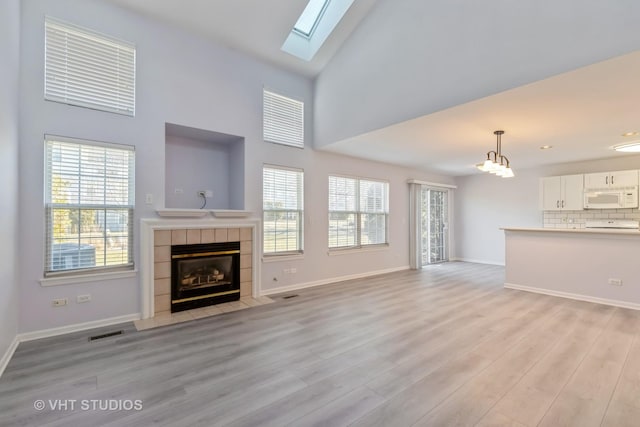 unfurnished living room with a fireplace, high vaulted ceiling, light hardwood / wood-style floors, and an inviting chandelier