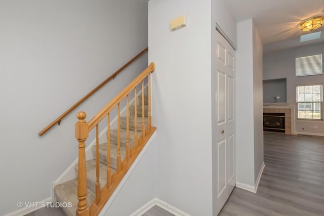 staircase with a tile fireplace and wood-type flooring