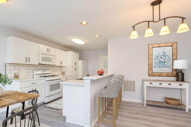 kitchen featuring white appliances, hanging light fixtures, a kitchen island with sink, white cabinets, and sink