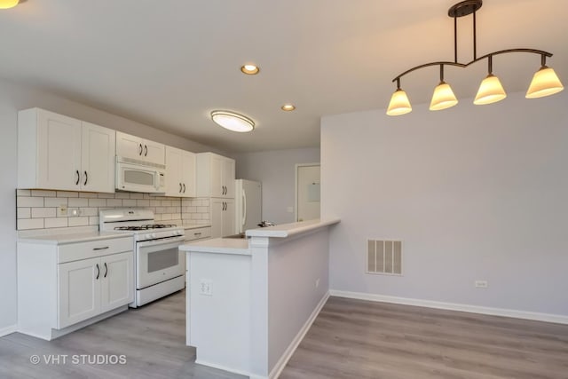 kitchen with white appliances, kitchen peninsula, decorative light fixtures, backsplash, and white cabinetry