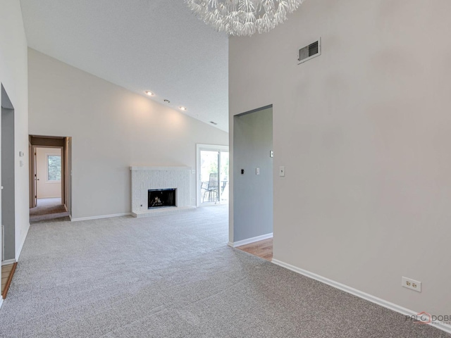 unfurnished living room with light carpet, high vaulted ceiling, a chandelier, and a brick fireplace