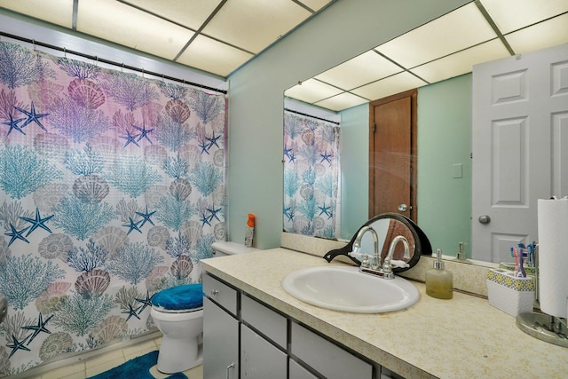 bathroom featuring toilet, vanity, tile patterned floors, and a drop ceiling