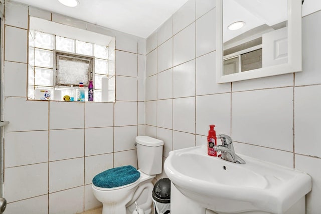 bathroom with sink, a shower with door, tile walls, and toilet