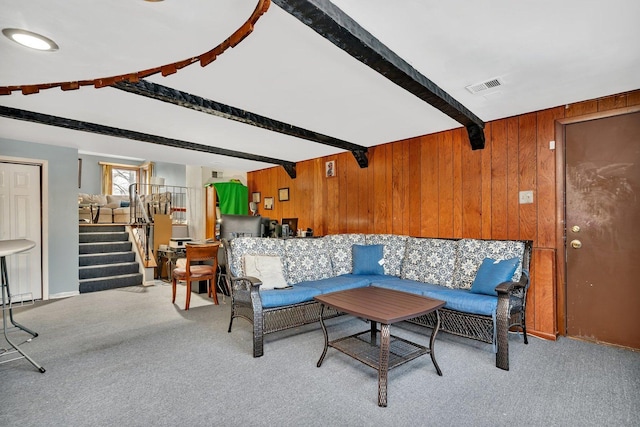 living room with wood walls, beam ceiling, and light colored carpet