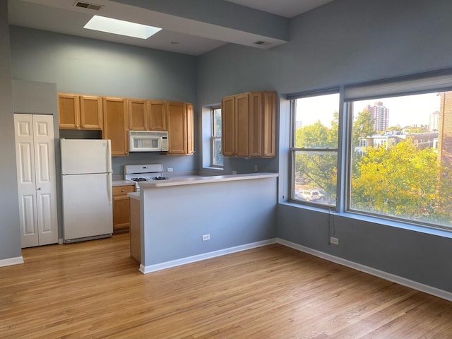 kitchen featuring a skylight, a high ceiling, kitchen peninsula, white appliances, and light wood-type flooring