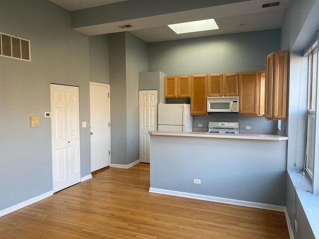 kitchen with kitchen peninsula, a skylight, white appliances, light hardwood / wood-style flooring, and a high ceiling