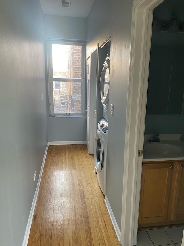 laundry room featuring light hardwood / wood-style floors, stacked washing maching and dryer, and sink