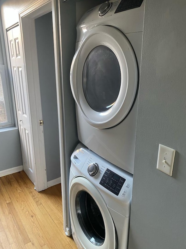 laundry room with light hardwood / wood-style flooring and stacked washing maching and dryer