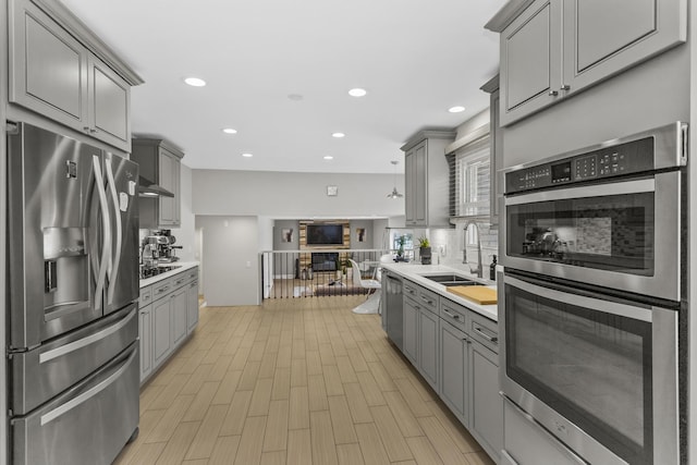 kitchen with appliances with stainless steel finishes, gray cabinetry, light hardwood / wood-style flooring, and sink