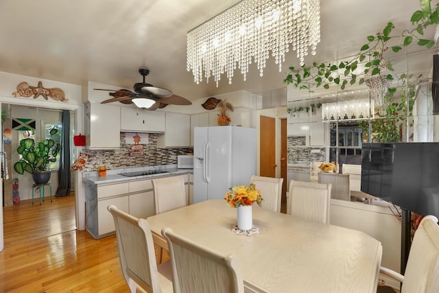 dining area with ceiling fan with notable chandelier and light hardwood / wood-style floors