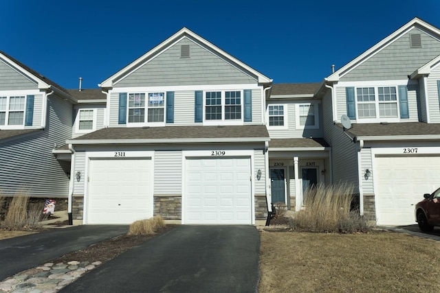 townhome / multi-family property featuring a garage, stone siding, and driveway