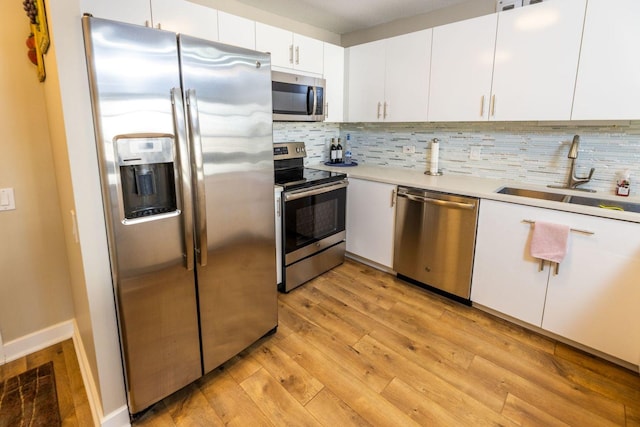 kitchen with sink, white cabinetry, light wood-type flooring, appliances with stainless steel finishes, and backsplash