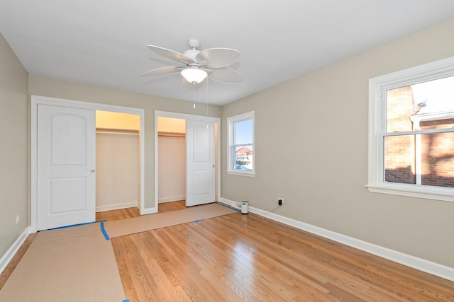 unfurnished bedroom featuring multiple closets, light wood-type flooring, and ceiling fan