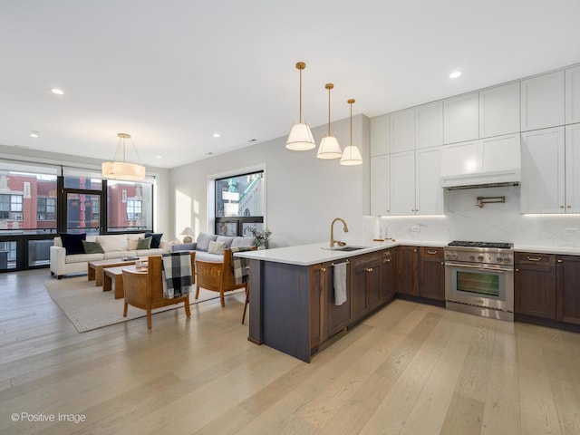 kitchen featuring dark brown cabinetry, stainless steel range, sink, hanging light fixtures, and light wood-type flooring