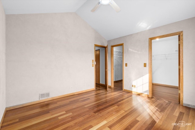 unfurnished bedroom with a walk in closet, ceiling fan, a closet, and vaulted ceiling