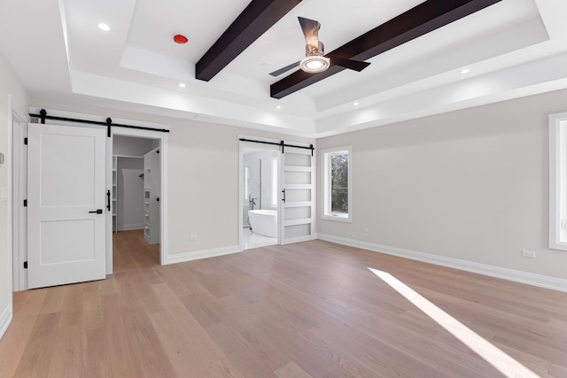 unfurnished bedroom featuring a raised ceiling, a barn door, ceiling fan, and ensuite bath