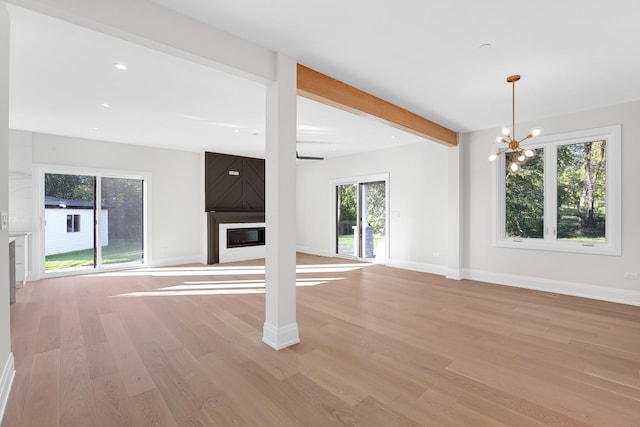 unfurnished living room featuring beamed ceiling, a notable chandelier, a large fireplace, and light hardwood / wood-style floors