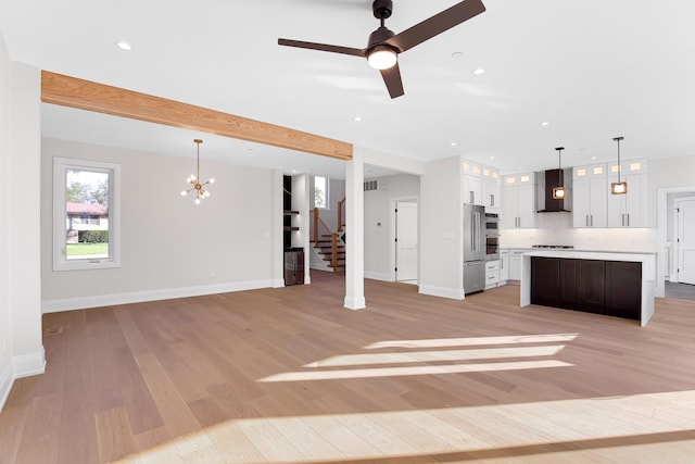 unfurnished living room with beam ceiling, ceiling fan with notable chandelier, and light hardwood / wood-style floors