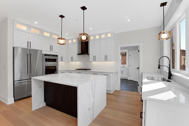 kitchen featuring stainless steel appliances, wall chimney range hood, a kitchen island, pendant lighting, and white cabinets