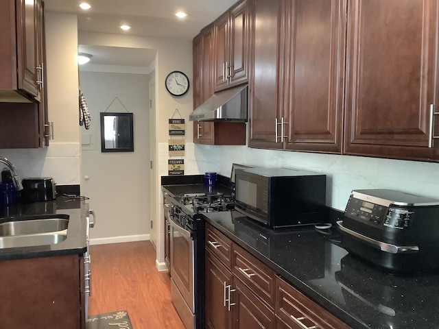 kitchen featuring dark stone countertops, stainless steel range with gas cooktop, sink, and light wood-type flooring