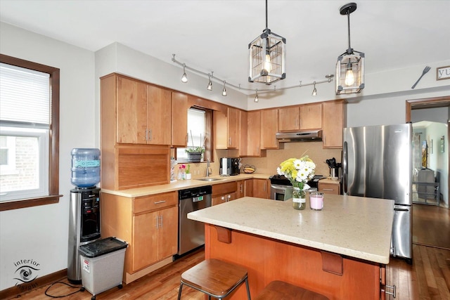 kitchen featuring sink, hanging light fixtures, a kitchen bar, appliances with stainless steel finishes, and light wood-type flooring