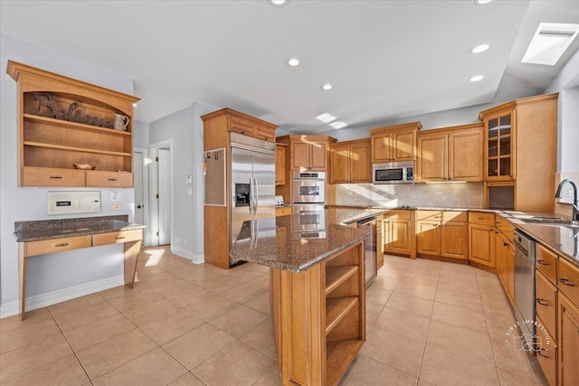 kitchen featuring decorative backsplash, a skylight, dark stone counters, a kitchen island, and appliances with stainless steel finishes