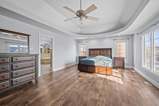 bedroom with hardwood / wood-style floors, a raised ceiling, ceiling fan, and ensuite bath