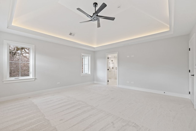 unfurnished room with ceiling fan, a raised ceiling, and light colored carpet