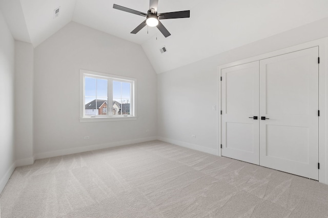 unfurnished bedroom with ceiling fan, a closet, light colored carpet, and vaulted ceiling