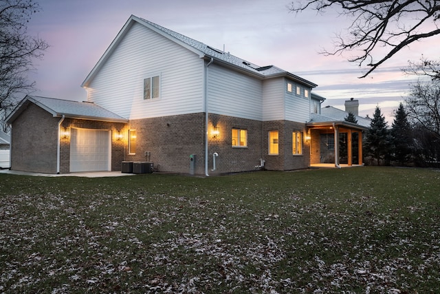 back house at dusk featuring a yard, a garage, and cooling unit