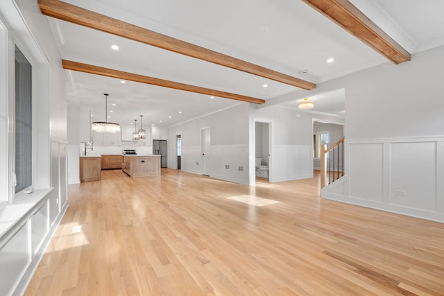 unfurnished living room featuring beam ceiling, light hardwood / wood-style floors, and ornamental molding