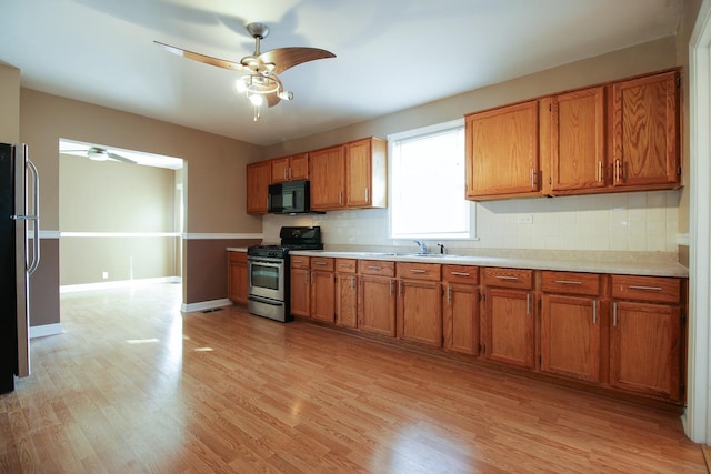 kitchen with ceiling fan, sink, stainless steel appliances, decorative backsplash, and light wood-type flooring