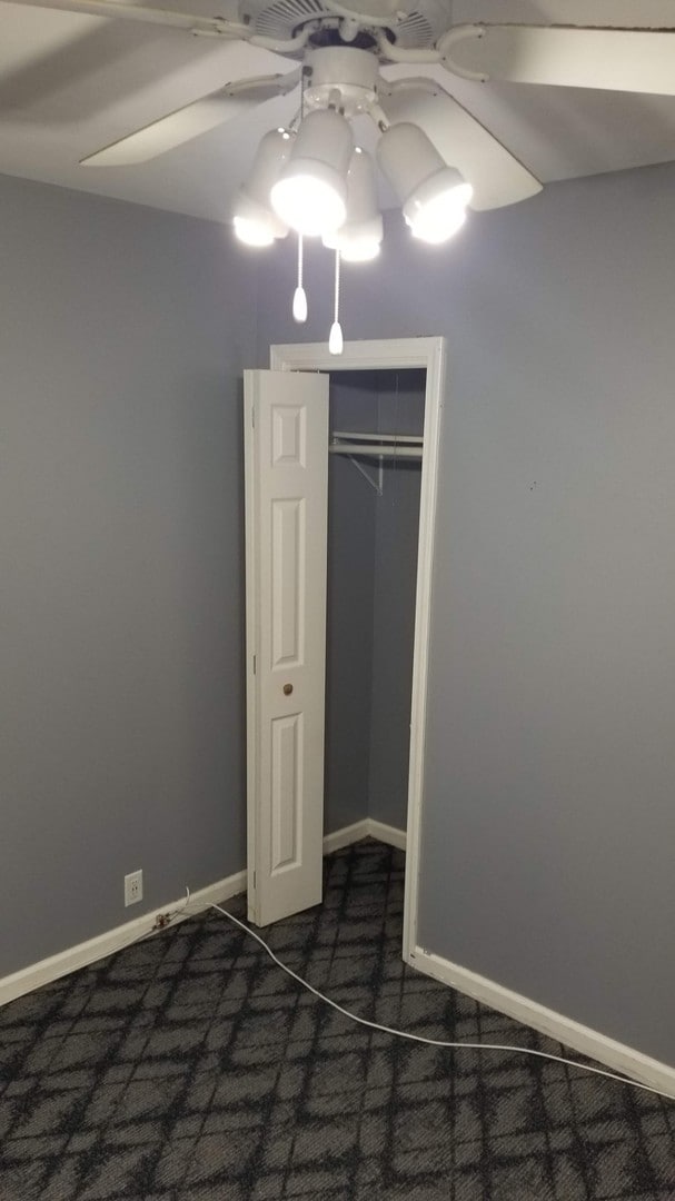 unfurnished bedroom with a closet, dark carpet, and ceiling fan