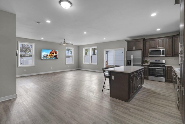 kitchen with a breakfast bar, appliances with stainless steel finishes, dark brown cabinets, a kitchen island, and wood-type flooring