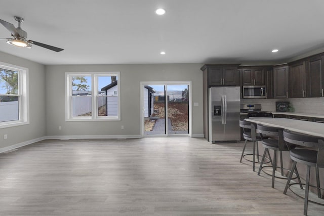 kitchen with backsplash, light wood-type flooring, dark brown cabinets, a kitchen bar, and stainless steel appliances