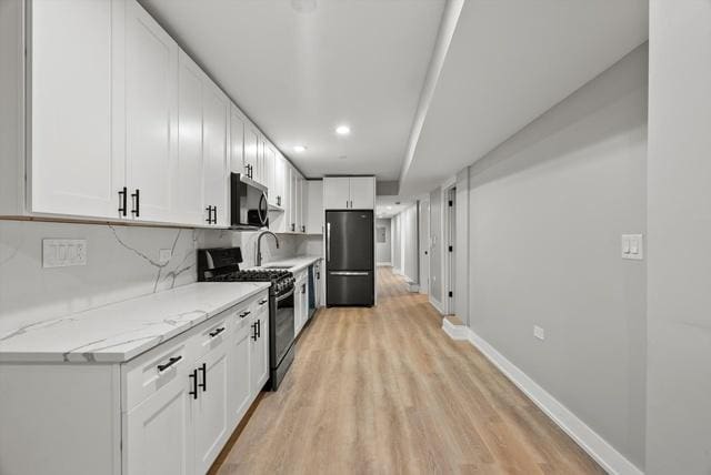 kitchen with tasteful backsplash, light stone counters, stainless steel appliances, light hardwood / wood-style flooring, and white cabinets