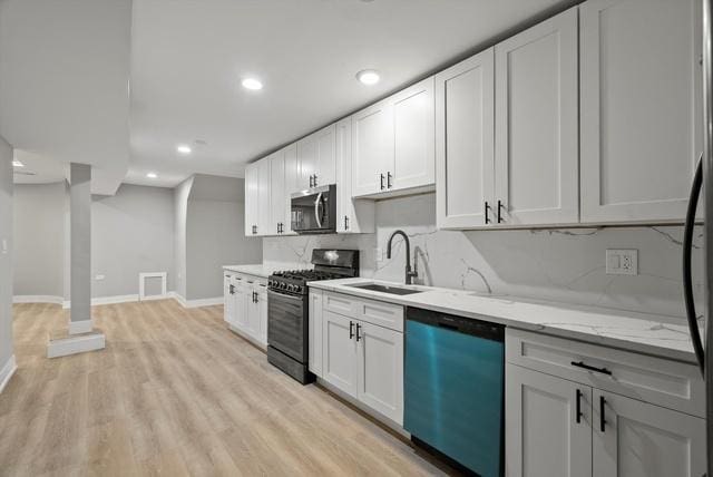 kitchen featuring dishwasher, sink, black gas range oven, light stone counters, and white cabinets