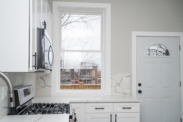 kitchen with backsplash, light stone countertops, white cabinets, and range with gas cooktop