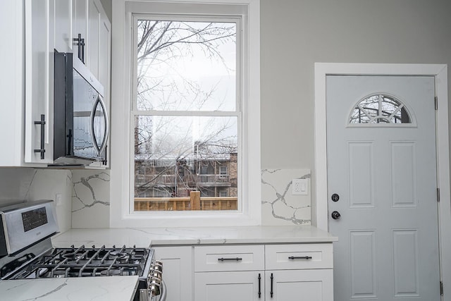 kitchen with light stone counters, white cabinetry, backsplash, and appliances with stainless steel finishes