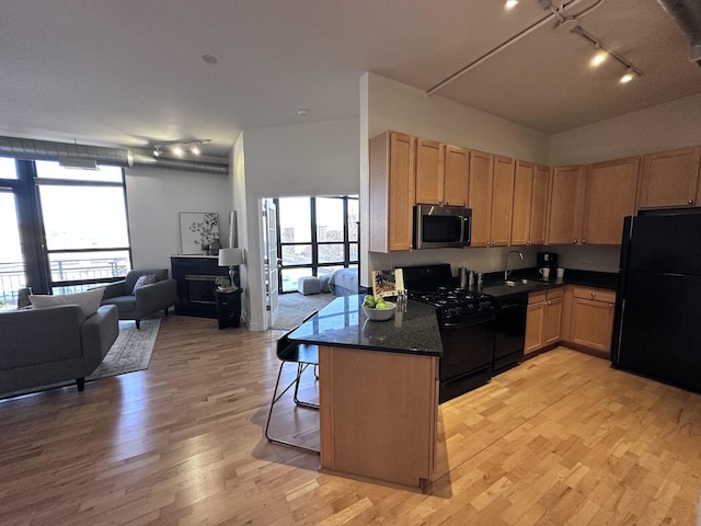 kitchen with dark stone countertops, a breakfast bar area, black appliances, kitchen peninsula, and sink