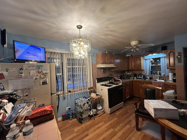 kitchen with hanging light fixtures, light hardwood / wood-style flooring, refrigerator, ceiling fan with notable chandelier, and white gas range oven