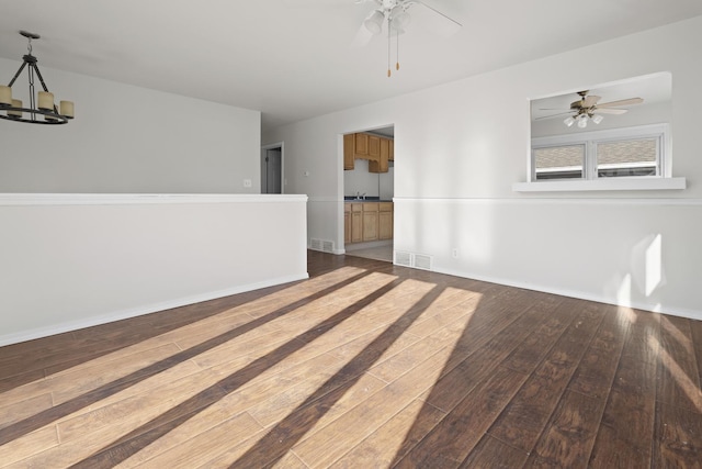 empty room with dark wood-type flooring, ceiling fan with notable chandelier, and sink