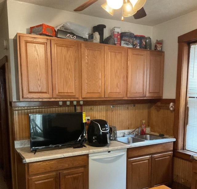 kitchen featuring sink, white dishwasher, wood walls, and ceiling fan