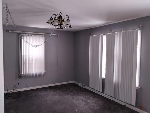 carpeted spare room featuring an inviting chandelier