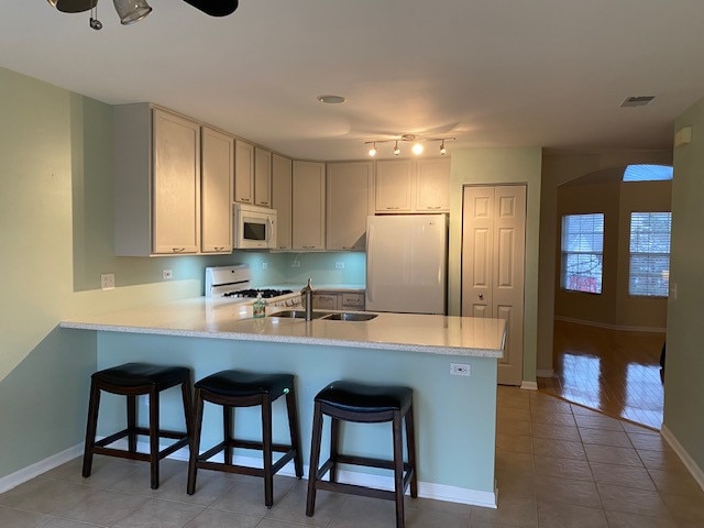 kitchen with kitchen peninsula, a kitchen bar, white appliances, sink, and light tile patterned floors