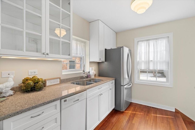 kitchen with light stone countertops, white cabinets, sink, wood-type flooring, and dishwasher