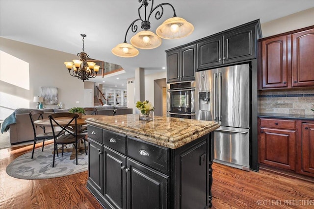 kitchen with appliances with stainless steel finishes, dark hardwood / wood-style flooring, tasteful backsplash, decorative light fixtures, and a kitchen island