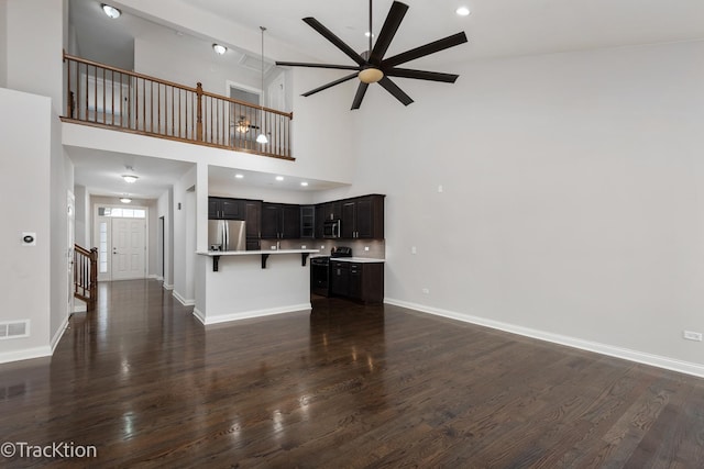 unfurnished living room featuring dark hardwood / wood-style floors, ceiling fan, and a high ceiling