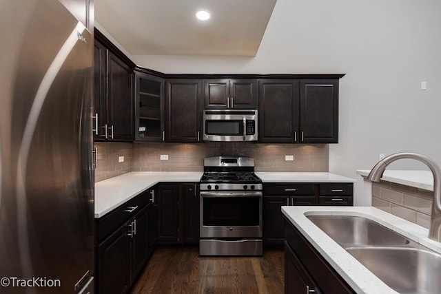 kitchen with decorative backsplash, appliances with stainless steel finishes, dark brown cabinets, dark wood-type flooring, and sink